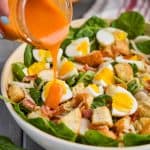 woman's handing pouring a mason jar full of red spinach salad dressing onto a spinach bacon salad with hard boiled eggs and croutons in a white bowl - 5