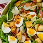 overhead view of spinach bacon salad with hard boiled eggs, croutons, water chestnuts in a white bowl