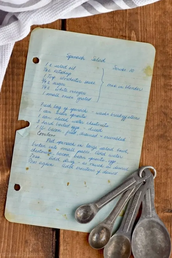 An overhead photo of a piece of paper with a spinach salad recipe and measuring spoons. 