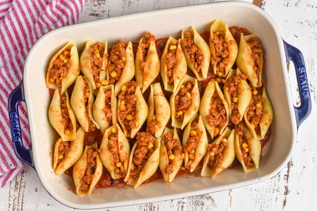 overhead of a pan of pasta shells stuffed with taco filling before they are covered with salsa and cheese
