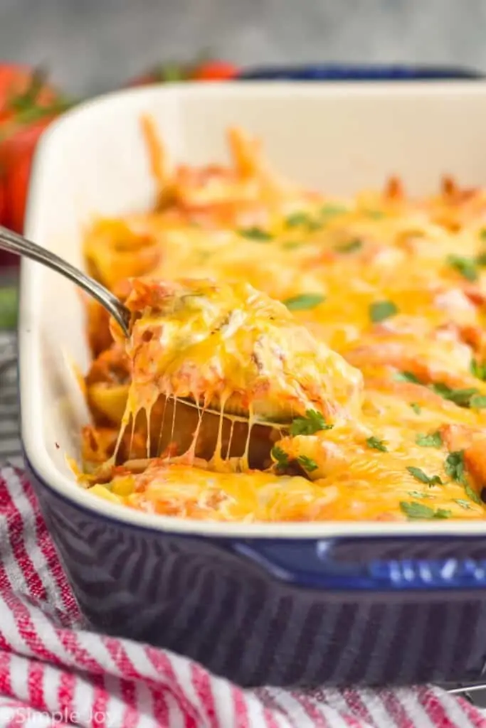 a stuffed shell filled with taco filling being lifted out of a casserole dish