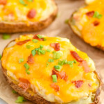a twice baked potato garnished with green onions and bacon on a piece of parchment paper - 11