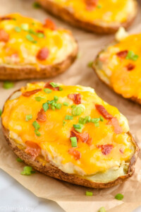 a twice baked potato garnished with green onions and bacon on a piece of parchment paper