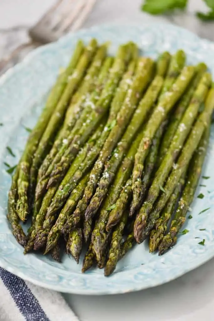 oven baked asparagus soon a blue platee sprinkled with parsley and parmesan