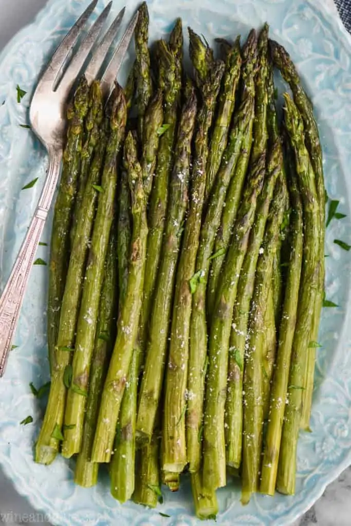 blue oval plate with oven roasted asparagus and vintage serving fork underneath 