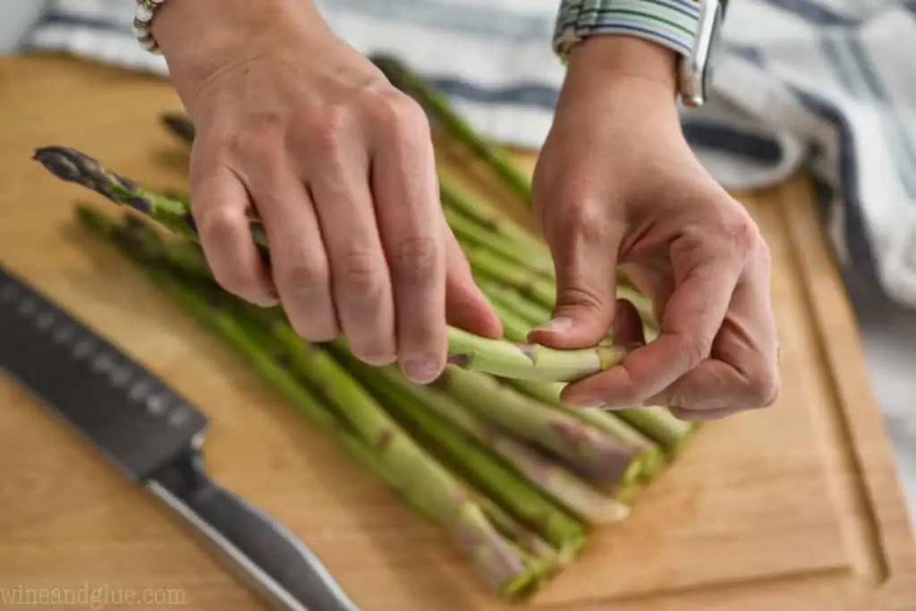 woman holding asparagus and snapping the bottom part of the stem off