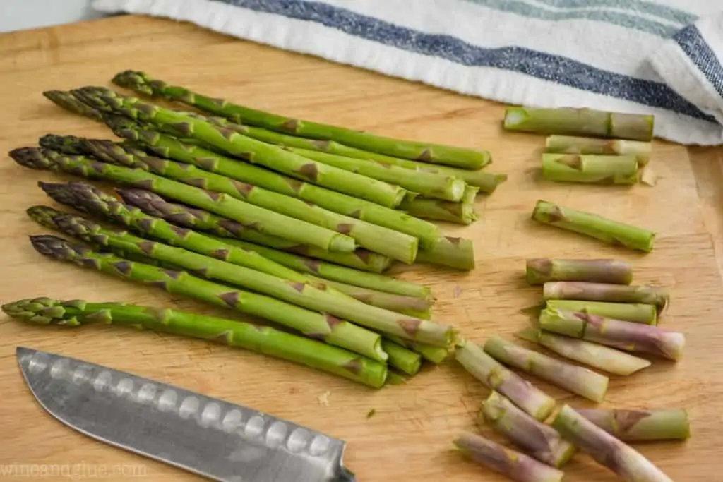 bunch of asparagus on a wood cutting board with woody bottoms snapped off to make oven roasted asparagus