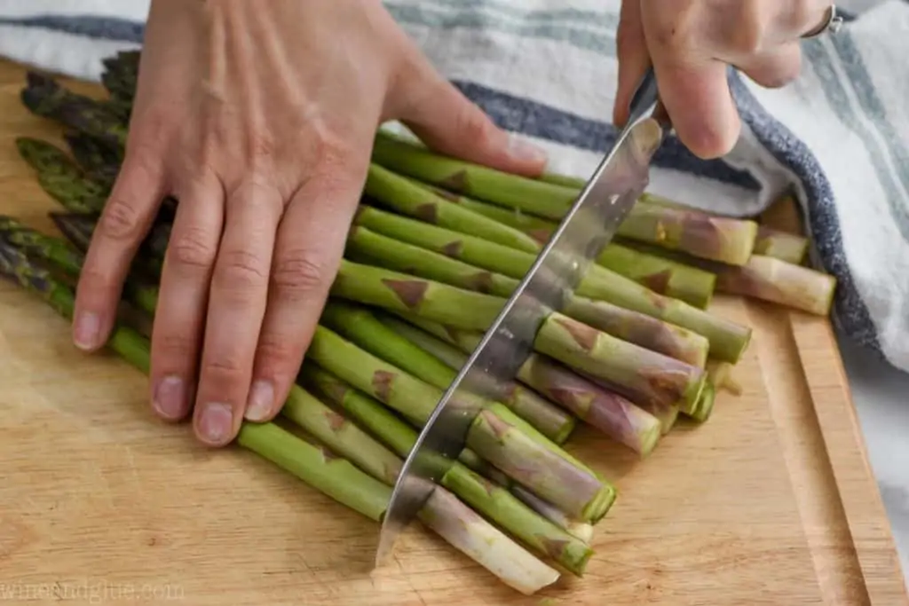 woman using a knife to cut off the woody bottoms of asparagus