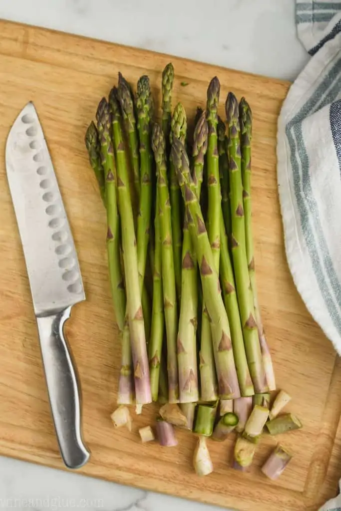 a bunch of asparagus on a cutting board with a small amount cut off the bottoms