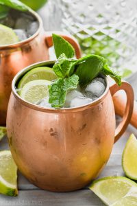 moscow mule with gin in copper mug garnished with mint and lime