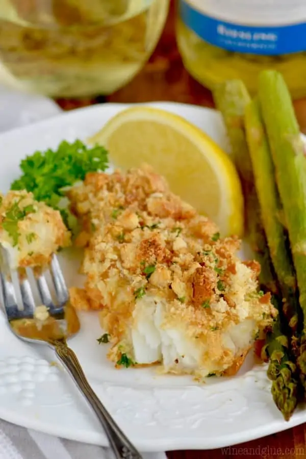 baked fish that is breaded with a side of asparagus and a slice of lemon