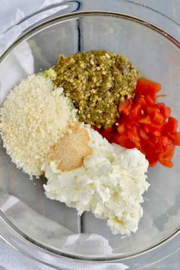 In a clear bowl, the ingredients of the cream cheese of the Pesto Cream Cheese Pinwheels. (cream cheese, parmesan, roasted red peppers, spices, and of course pesto)