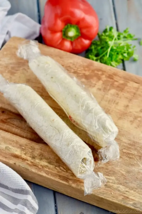 Rolled up, the Pesto Cream Cheese Pinwheels are wrapped by cling wrap. 