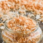 pinterest graphic of a small mason jar full of toasted coconut on a tray with more toasted coconut, says: "how to: toast coconut, simplejoy.com"