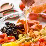 pinterest graphic of pouring italian dressing over a bowl of ingredients for Italian pasta salad, says: the best italian pasta salad