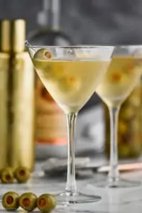 straight on view of a frosted martini glass with a dirty martini in it, garnished with three olives