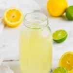 clear mason jar full of homemade sweet and sour mix with limes and lemons around it on marble counter top - 11