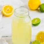clear mason jar full of homemade sweet and sour mix with limes and lemons around it on marble counter top