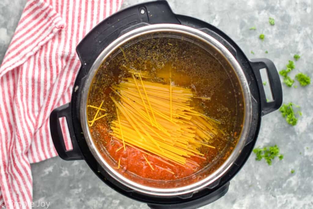 overhead of an instant pot with chicken stock, spaghetti sauce, and uncooked spaghetti
