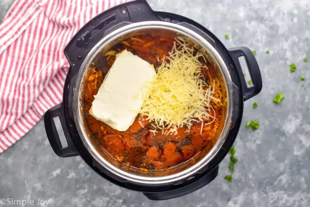 overhead of an instant pot filled with spaghetti sauce, a brick fo cream cheese, and Parmesan cheese