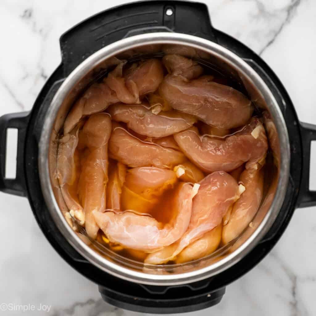 raw chicken tenders in chicken broth inside a pressure cooker