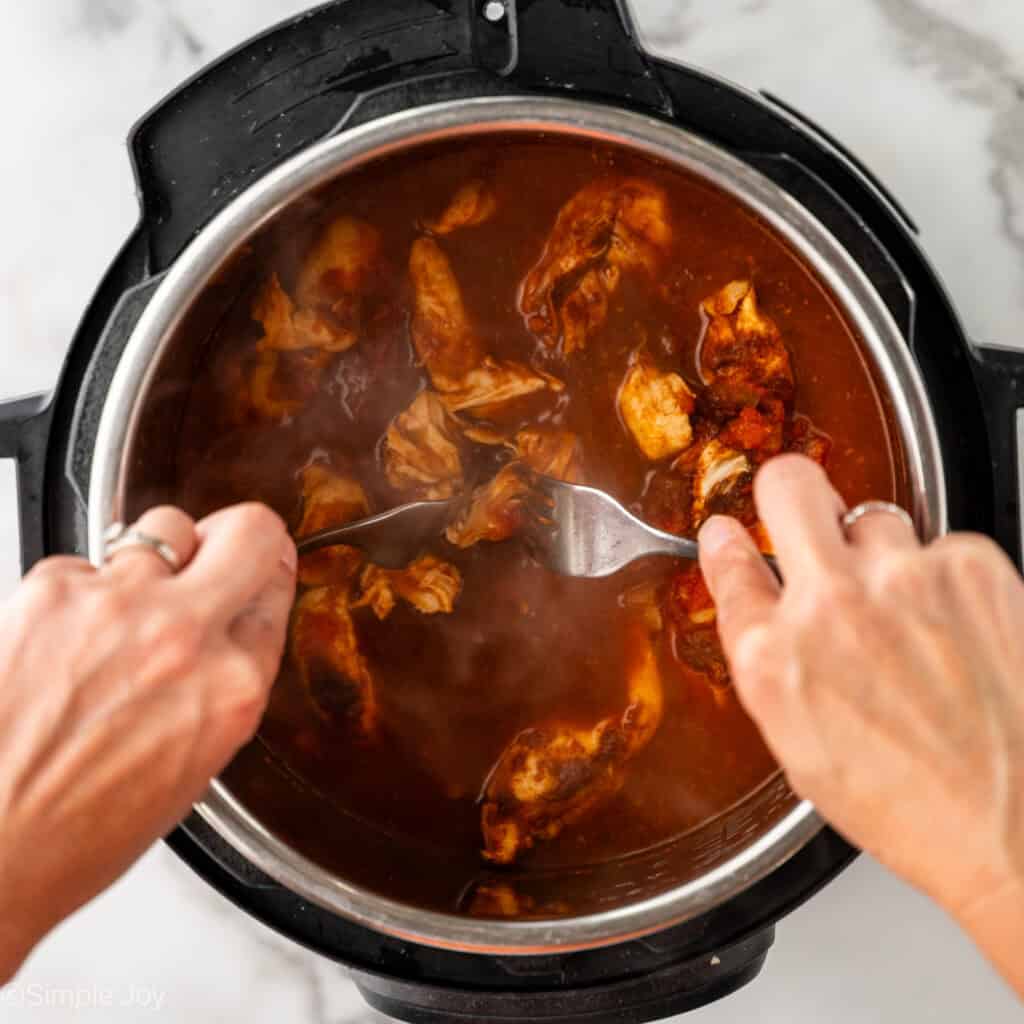 shredding chicken in a salsa and broth mixture inside an instant pot