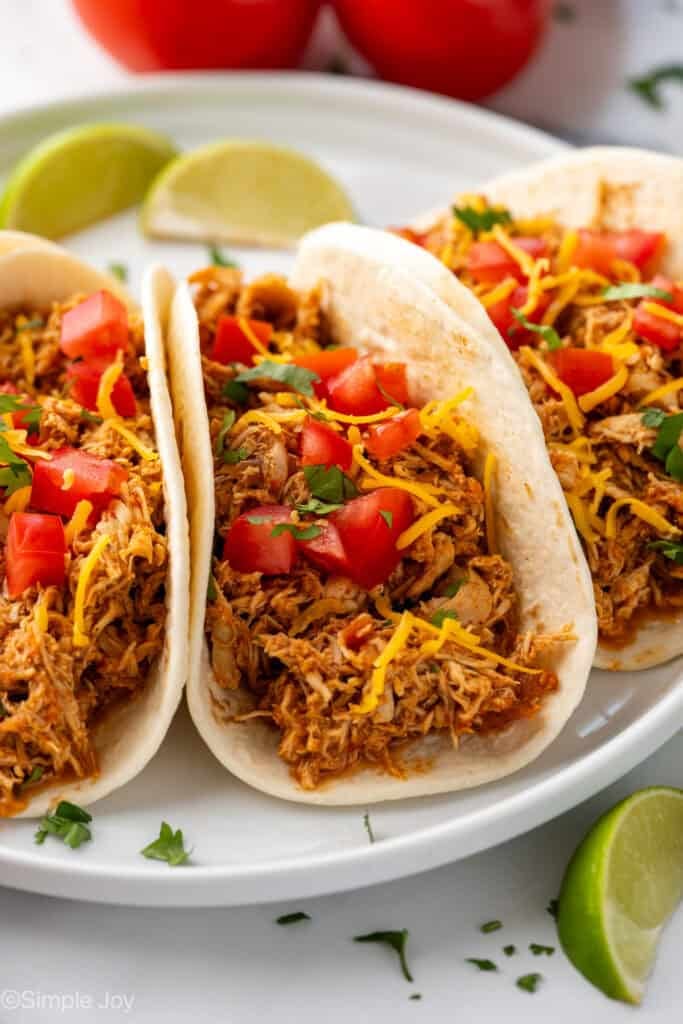 close up of three instant pot chicken tacos on a plate with diced tomatoes and shredded cheese