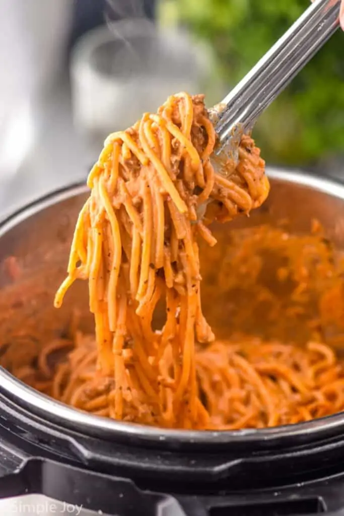 tongs lifting creamy spaghetti out of an instant pot