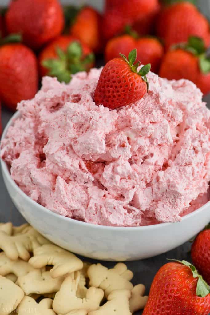bowl of strawberry fluff dip with a strawberry on top and a side of animal crackers