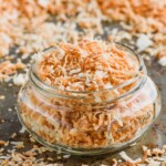 a small mason jar full of toasted coconut on a tray with more toasted coconut