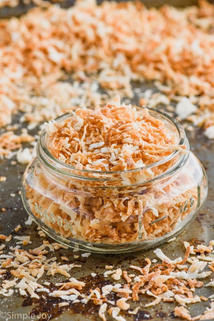 a small mason jar full of toasted coconut on a tray with more toasted coconut