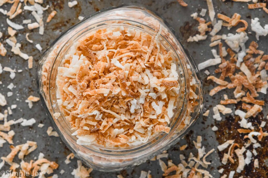 overhead of a small mason jar full of toasted coconut with coconut flakes around it