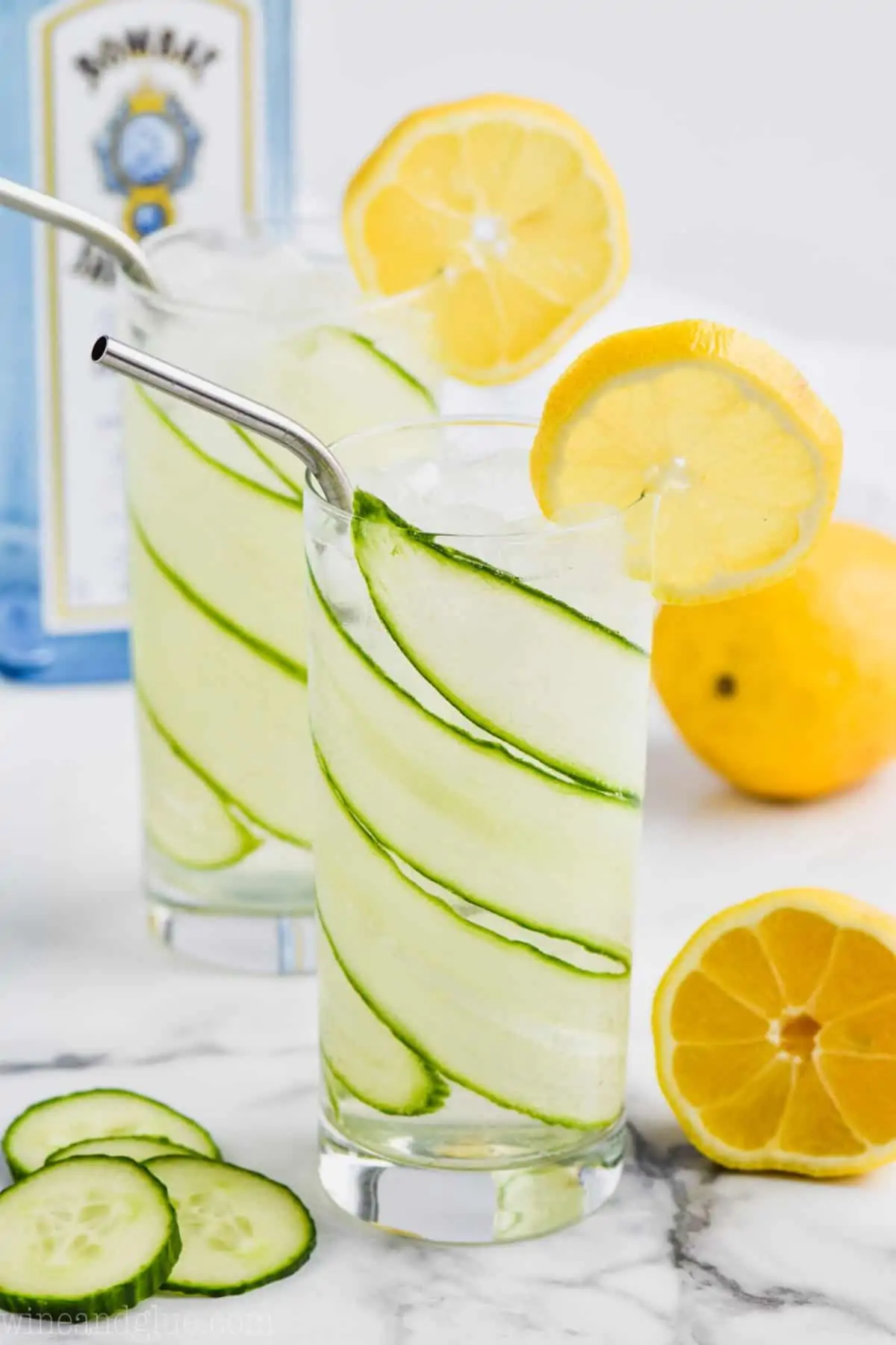 two glasses of cucumber lemon gin and tonic complete with thinly sliced cucumber lining the whole high ball glass and lemon slices garnishing the glasses