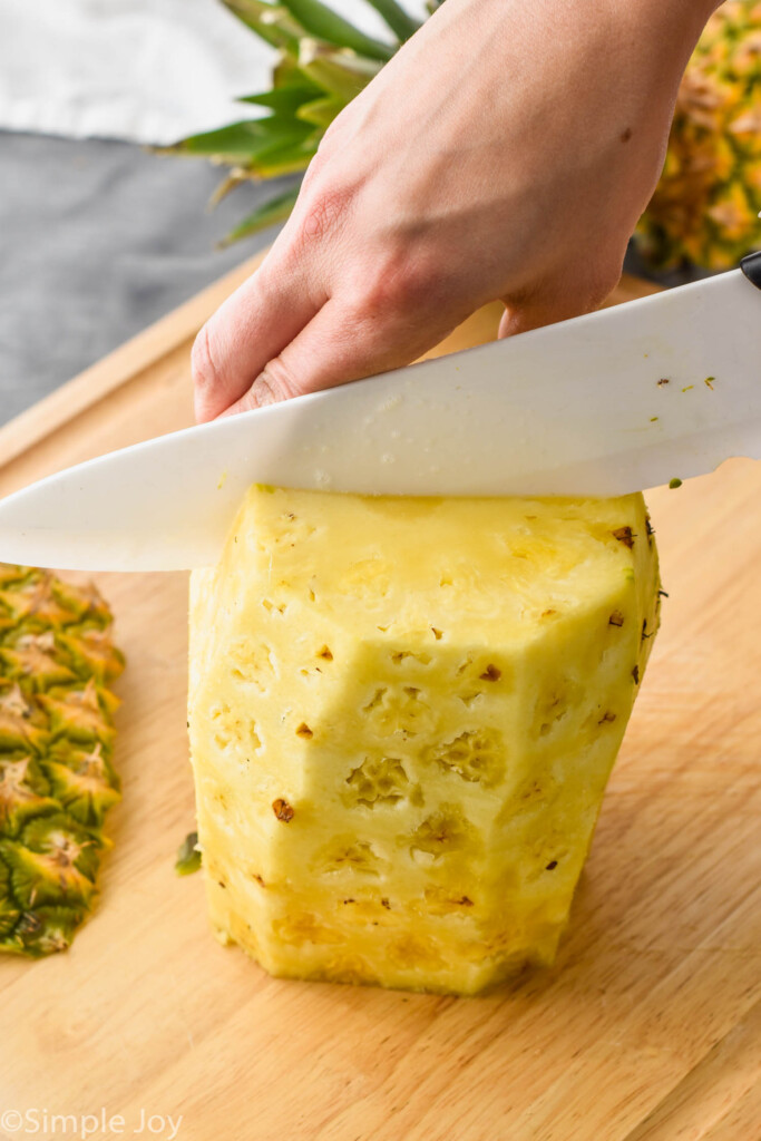 a pineapple, with the skin, top, and bottom gone, being cut in half