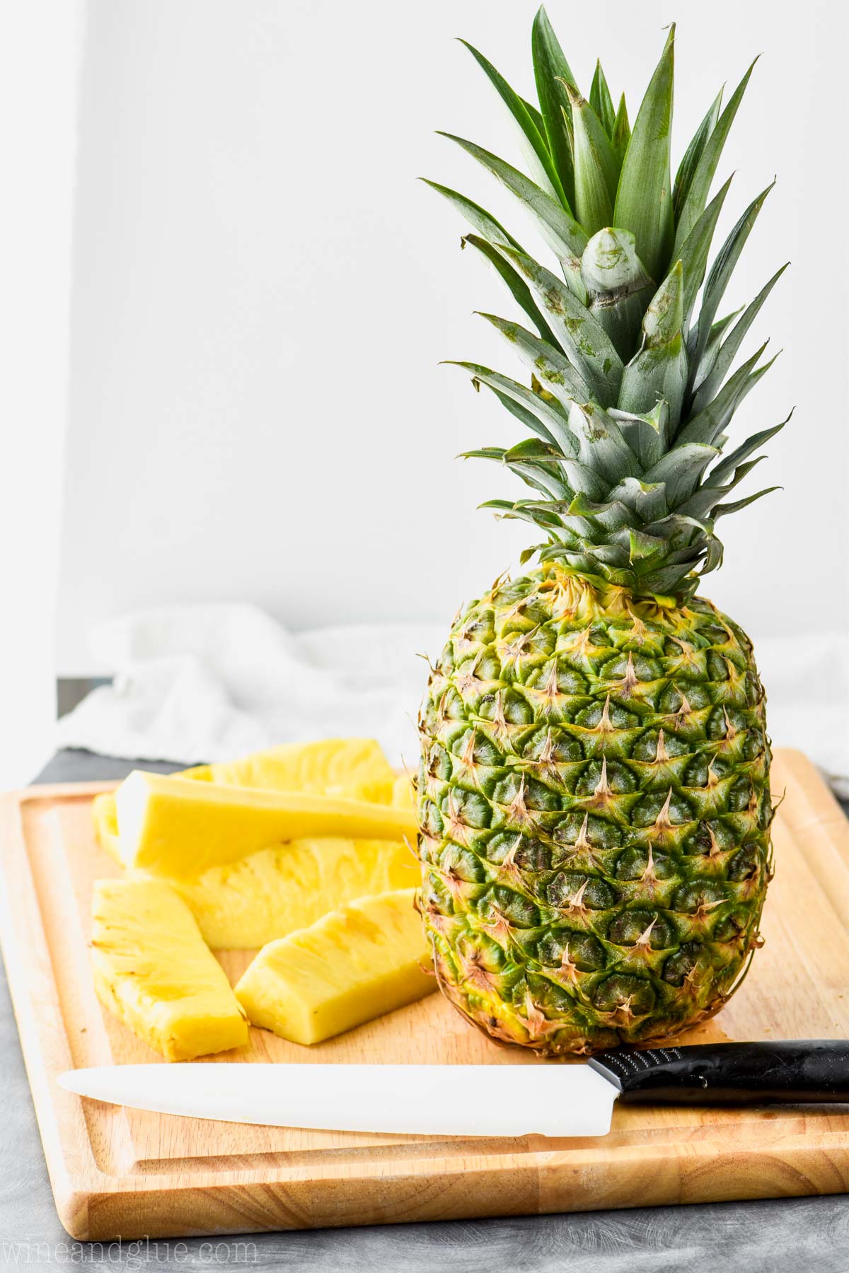 a pineapple sitting on a cutting board with slices of pineapple and a knife sitting next to it.