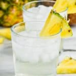 a tumbler full of ice and pina colada vodka soda, garnished with a pineapple wedge - 6