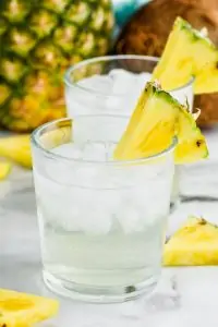 a tumbler full of ice and pina colada vodka soda, garnished with a pineapple wedge