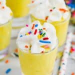 shot glass filled with birthday cake pudding shots, topped with whipped cream and rainbow sprinkles, three other filled shot glasses in the background - 6