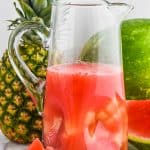 a tall pitcher of watermelon rum punch with a pineapple and a watermelon in the background - 5