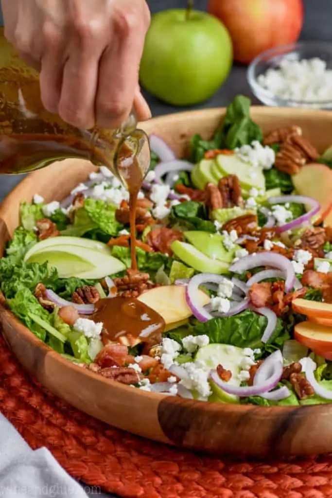 pouring dressing on an apple bacon salad