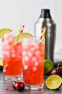 two high ball glasses with a cocktail shaker in the background filled with ice and cherry limeade recipe