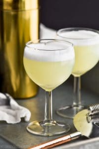 Straight on view of two wine goblets filled with gin fizz recipe and gold shaker in the background