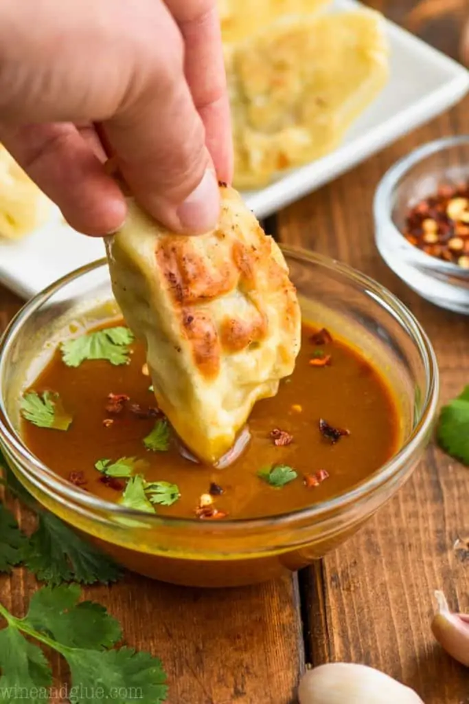 dipping a fried potsticker in potsticker sauce that is topped with red pepper flakes and cilantro