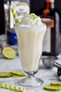 tall milkshake glass filled with margarita boozy milkshake with liquor bottles in the background garnished with lime zest