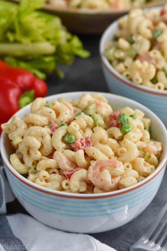A bowl of shrimp pasta salad that shows small cut pieces of red pepper, peas, small cut pieces of celery, and shrimp