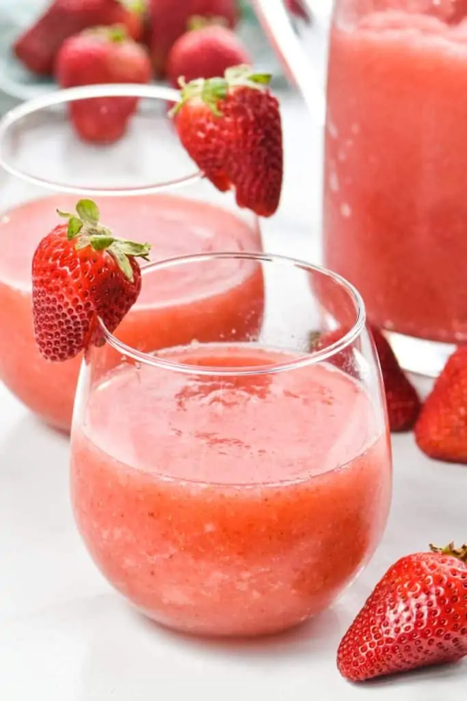 glass of strawberry wine slushie made in a blender with a sliced strawberry on the glass