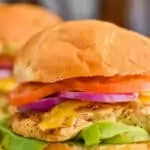 close up of a grilled chicken sandwich with lettuce on the bottom, then the chicken breast, then honey bbq sauce, then red onions and tomatoes