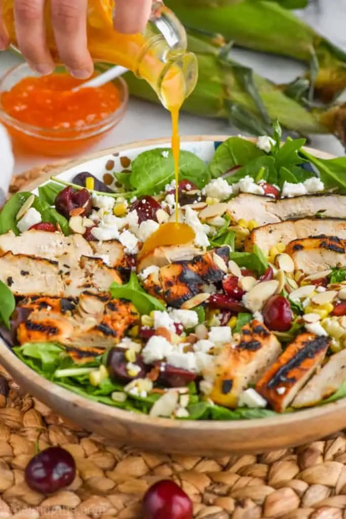 pouring salad dressing on a cherry and corn salad with grilled chicken