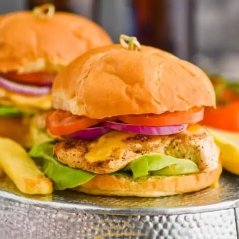 two grilled chicken sandwiches on a turned over metal tray with steak fries around them