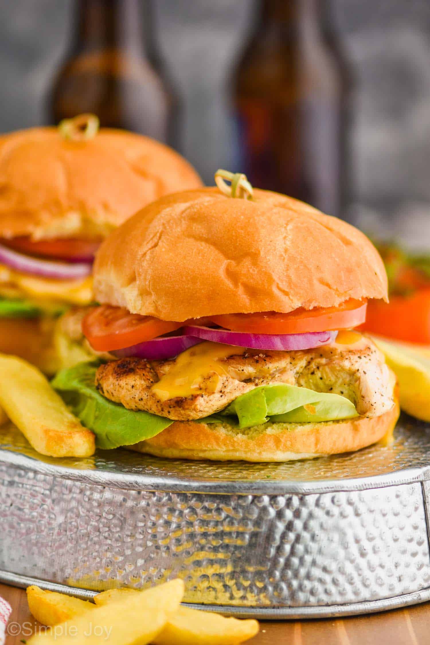 two grilled chicken sandwiches on a turned over metal tray with steak fries around them